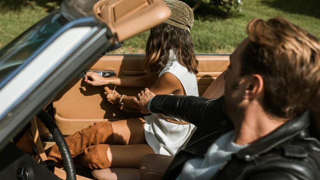 A man in a car holding a woman's arm as she reaches for the door handle.