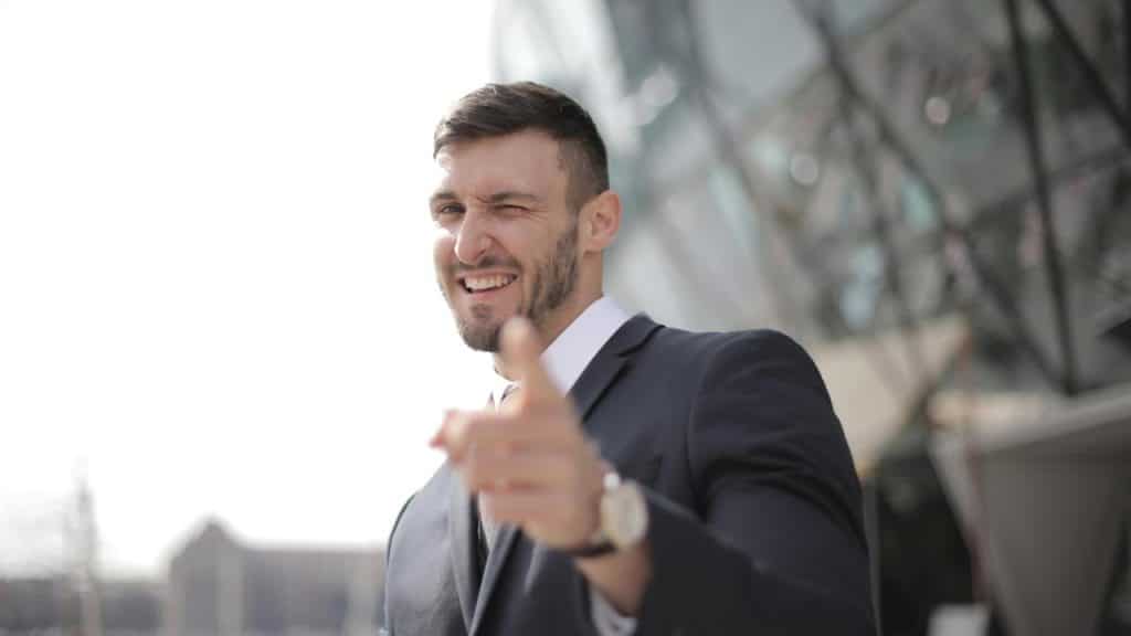 A man in a suit winking and pointing toward the camera.