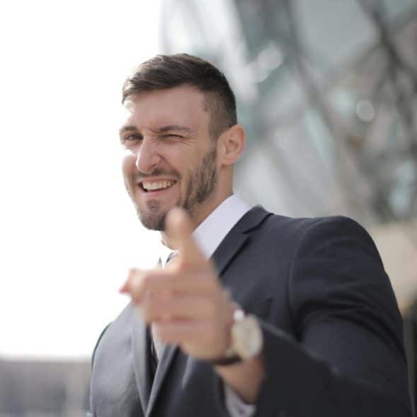A man in a suit winking and pointing toward the camera.