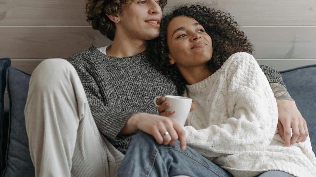 A couple sitting on a couch with the woman holding a white mug.