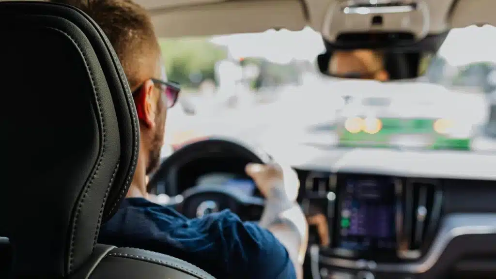 A man wearing sunglasses driving a car during the day.