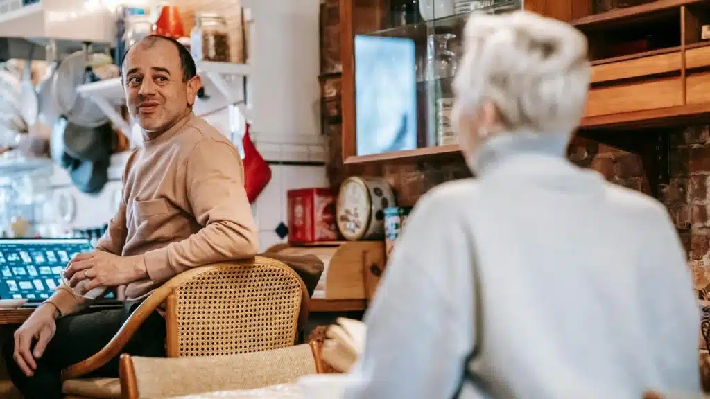 A man sitting at a kitchen table smiling while talking to a woman.