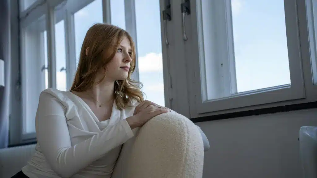A woman sitting by a window looking outside thoughtfully.