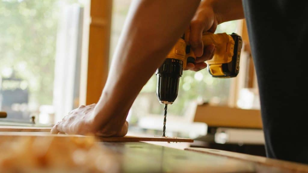 A person using a yellow power drill on a wooden surface.