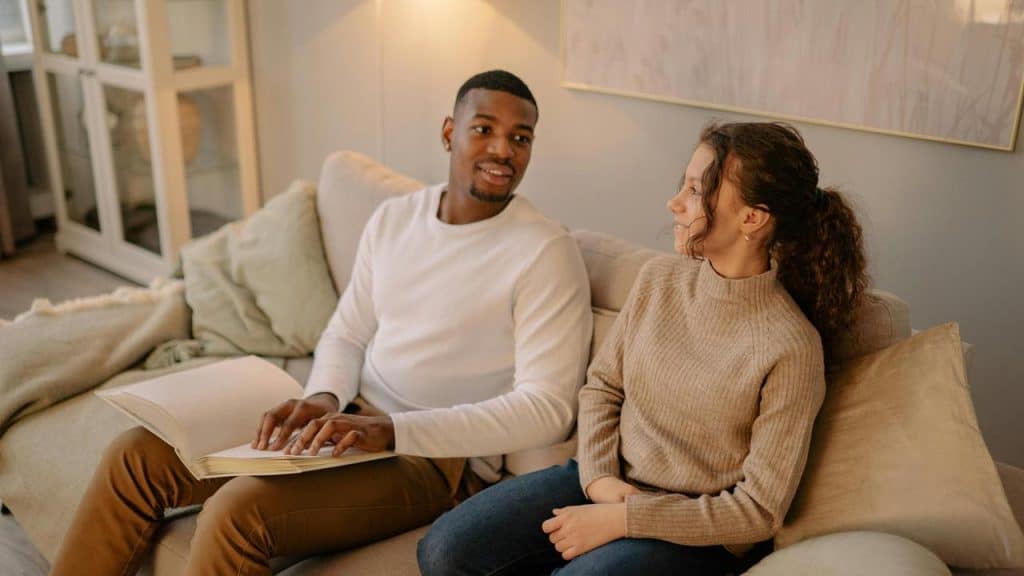 A man and a woman sitting on a couch talking and smiling.