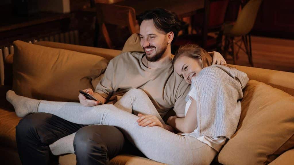 A couple sitting on a couch smiling while watching something together.