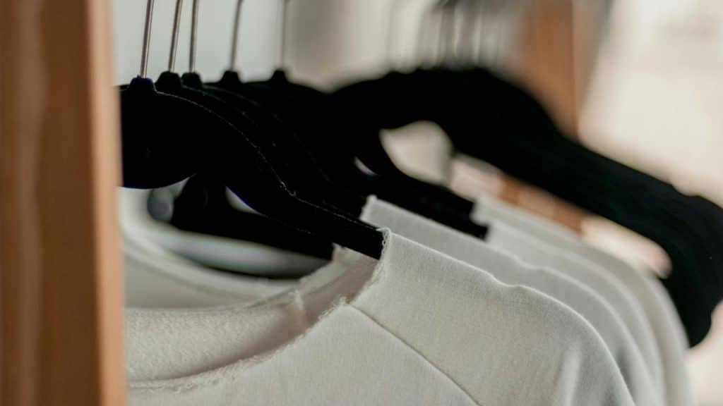 A row of white shirts hanging on black hangers in a closet.