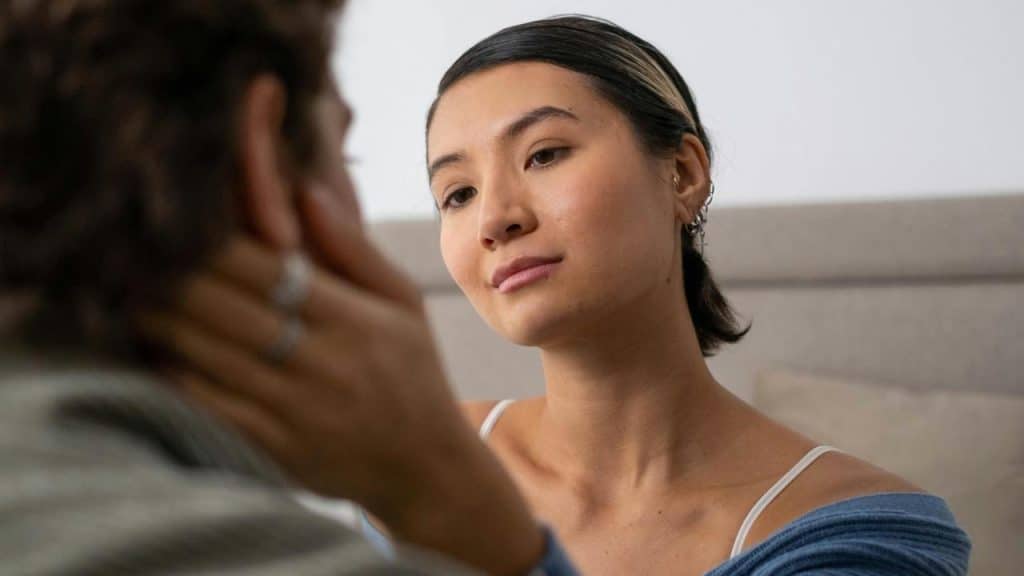 A woman looking at a man while holding his face gently.