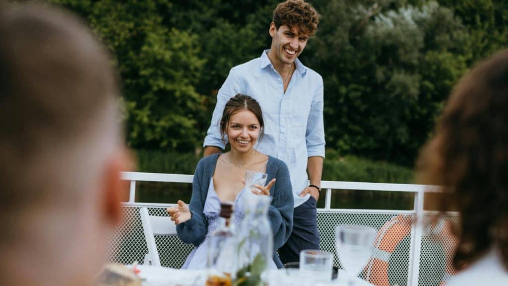 A smiling couple standing by an outdoor dining table with friends.