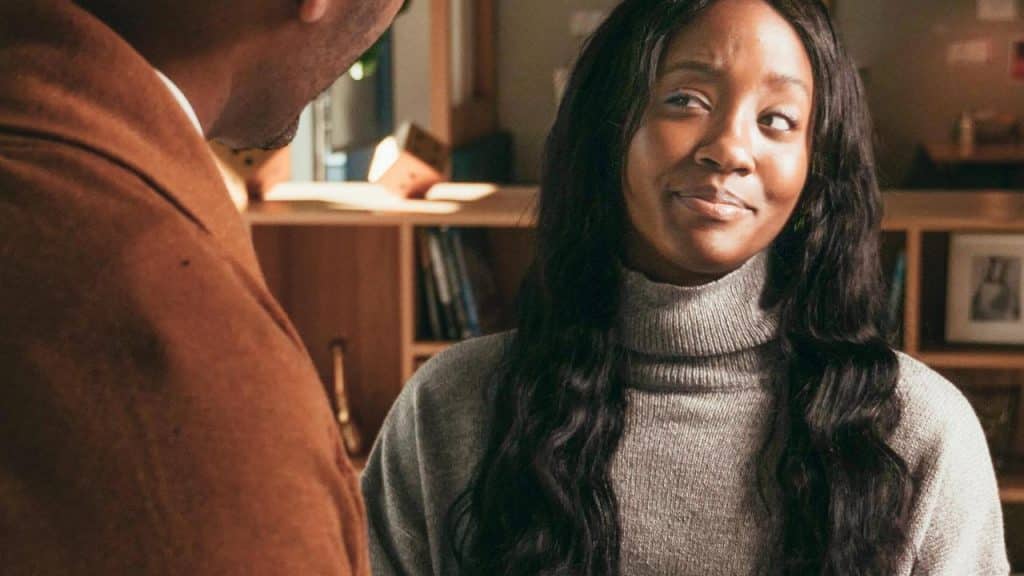 A woman smiling while talking to a man indoors.