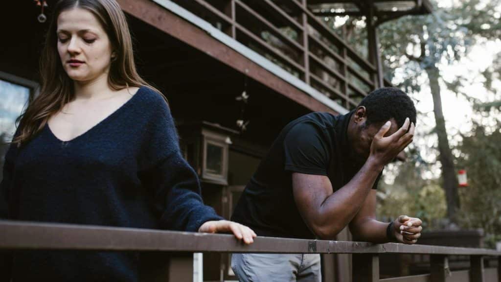 A woman walking away while a man leans on a railing with his hand covering his face.
