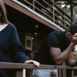A woman walking away while a man leans on a railing with his hand covering his face.