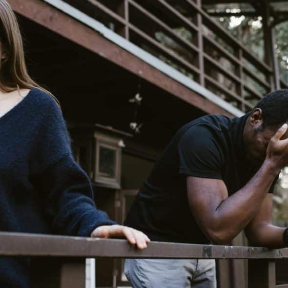 A woman walking away while a man leans on a railing with his hand covering his face.