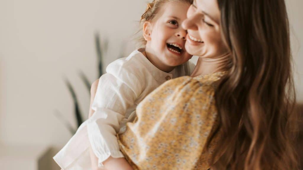 A mother smiling while holding her laughing daughter.