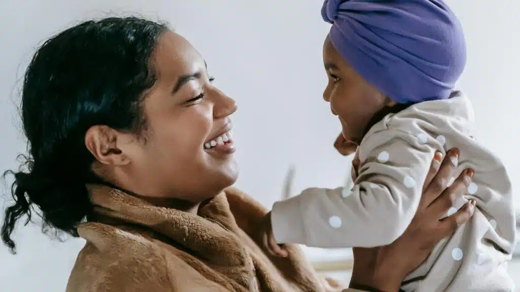 A mother smiling while holding her baby wearing a purple headwrap.