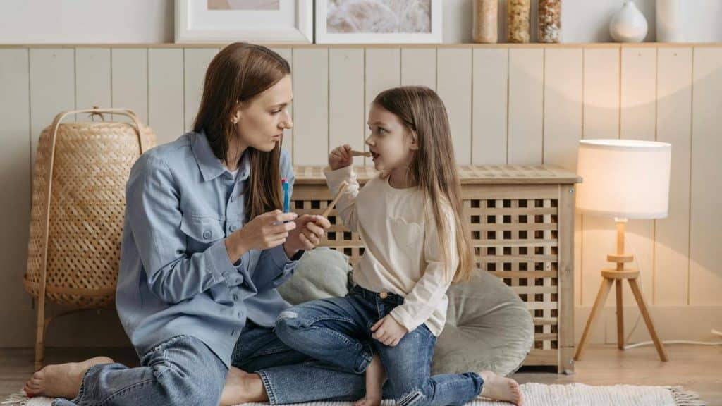 A mother teaching her daughter how to brush her teeth at home.