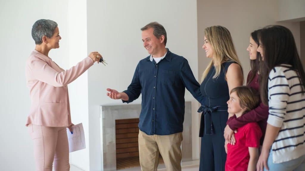 A real estate agent handing house keys to a smiling family inside their new home.