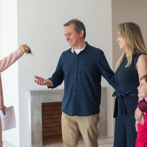A real estate agent handing house keys to a smiling family inside their new home.