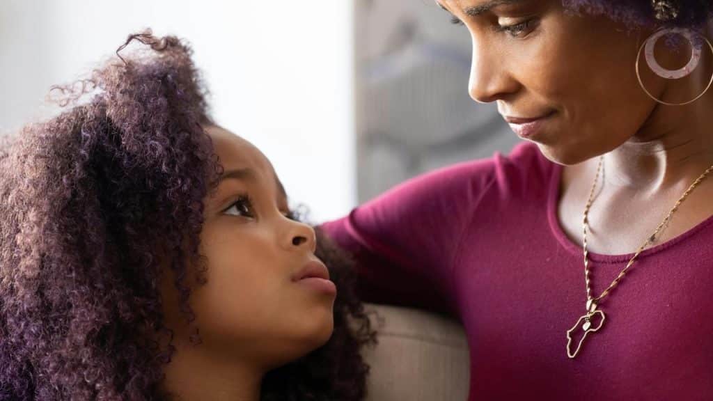 A mother gently talking to her daughter who looks thoughtful.