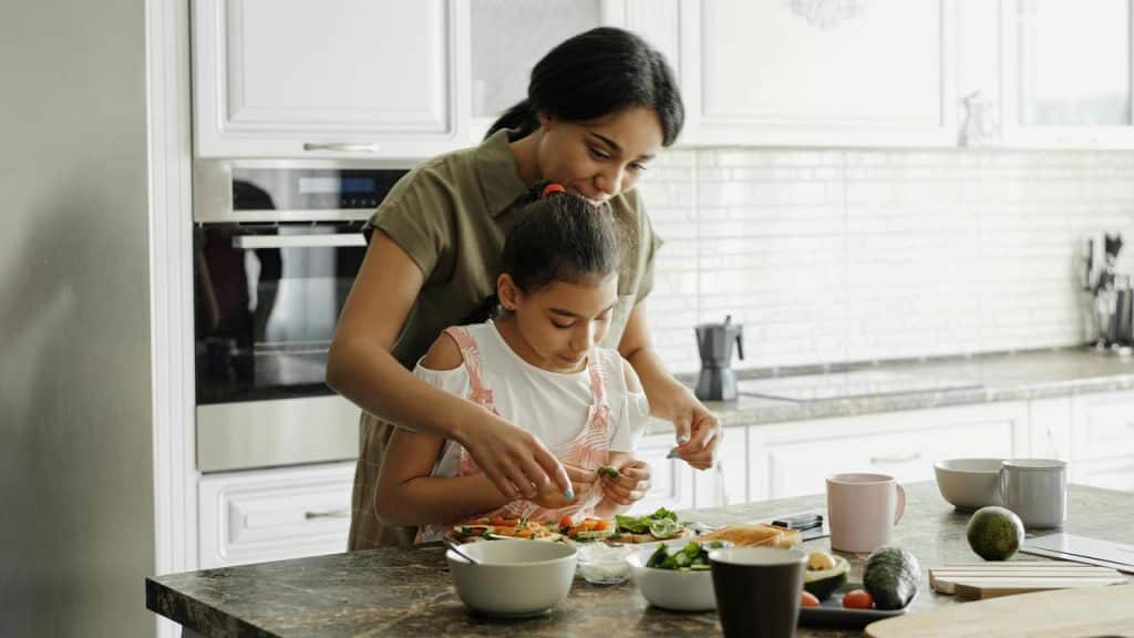 A mother helping her daughter prepare food in the kitchen.