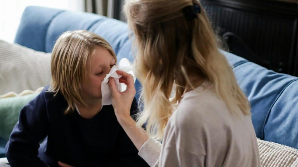 A mother wiping her sick son's nose with a tissue.