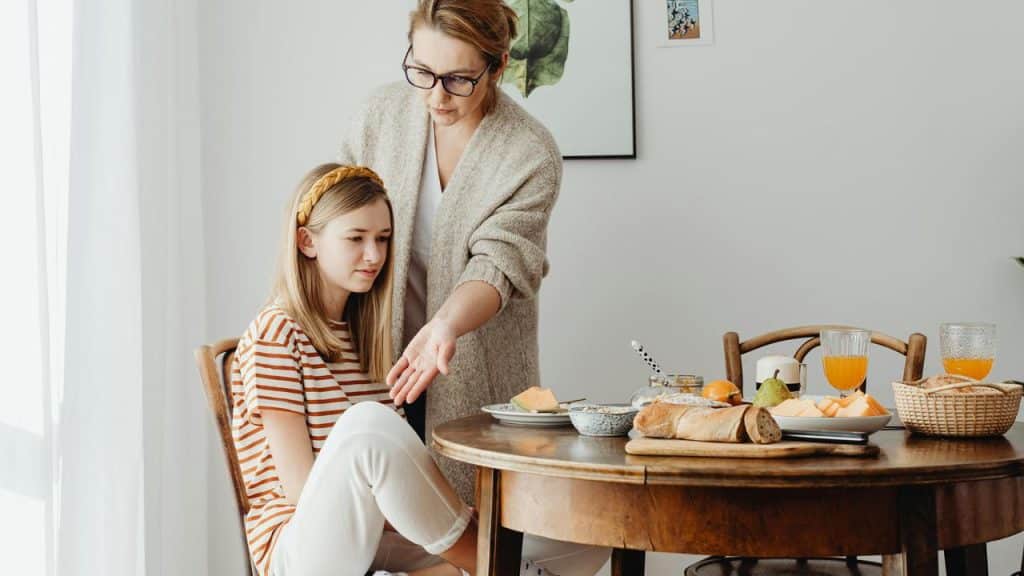 A mother comforting her daughter at the breakfast table.