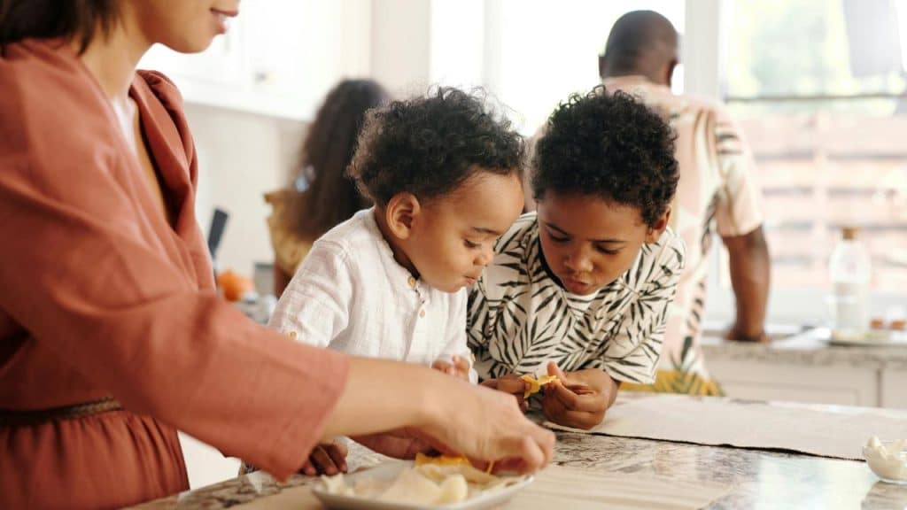 A mother preparing food with her two children in the kitchen.