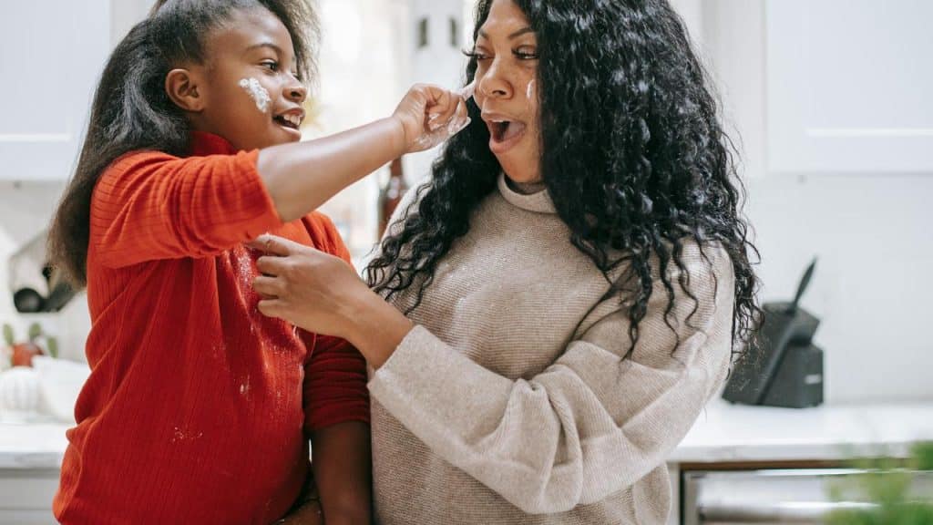 A mother and daughter playfully putting flour on each other while baking.