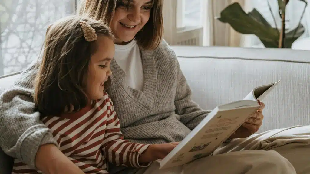 A mother reading a book with her daughter on the couch.