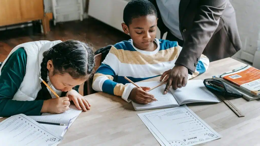 A person helping two children with their homework at a table.