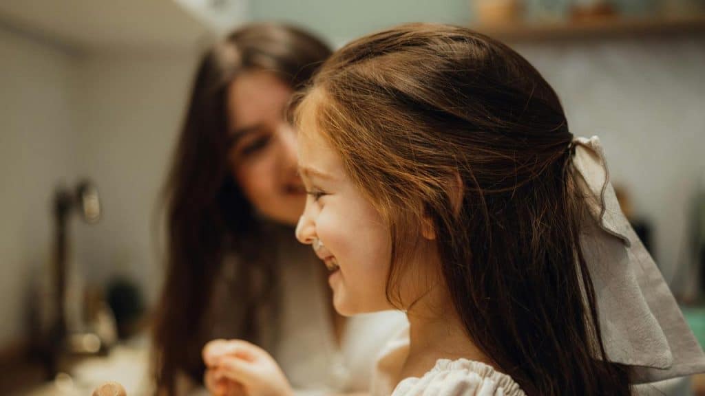 A mother smiling at her laughing daughter in the kitchen.