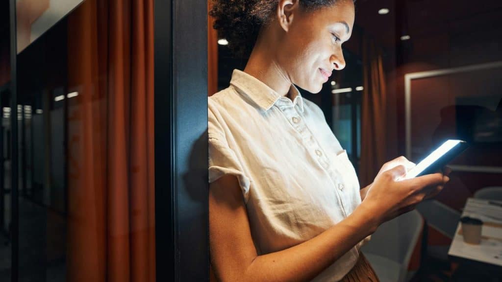 A woman smiling while using her smartphone indoors.
