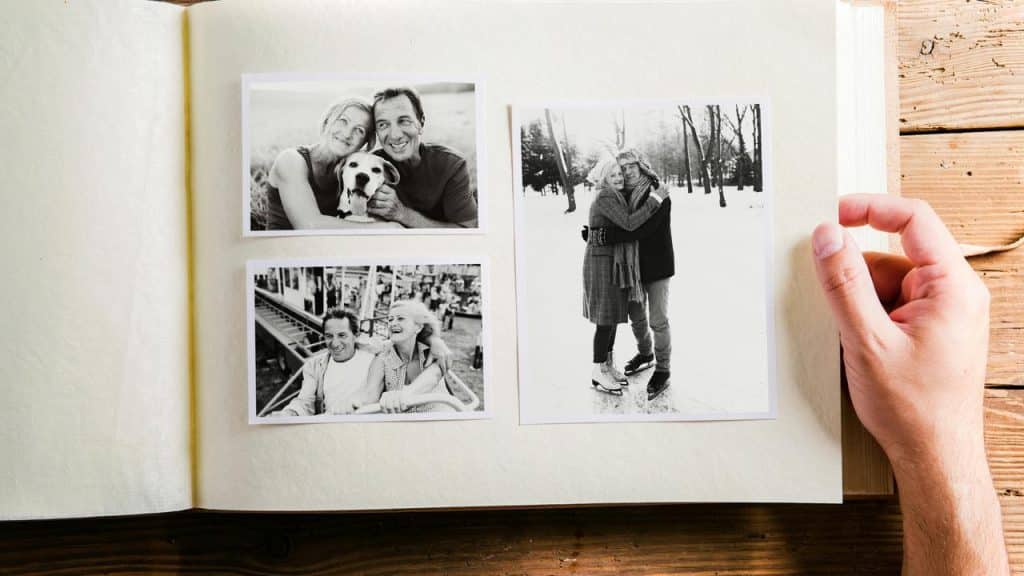A person holding a photo album with black and white pictures of an older couple.