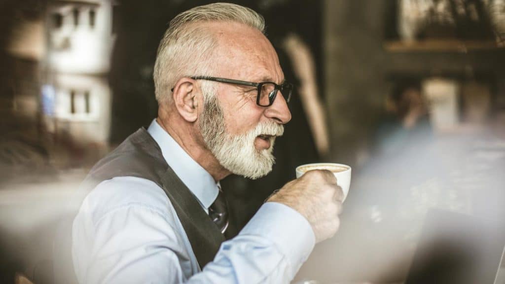 An older man with glasses drinking coffee in a café.