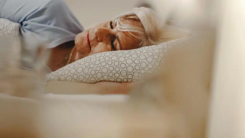 An older woman peacefully sleeping on a patterned pillow.