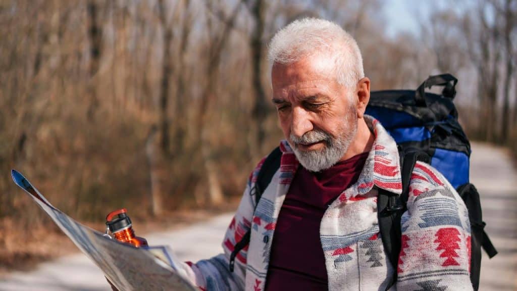 An older man with a backpack reading a map on a forest trail.