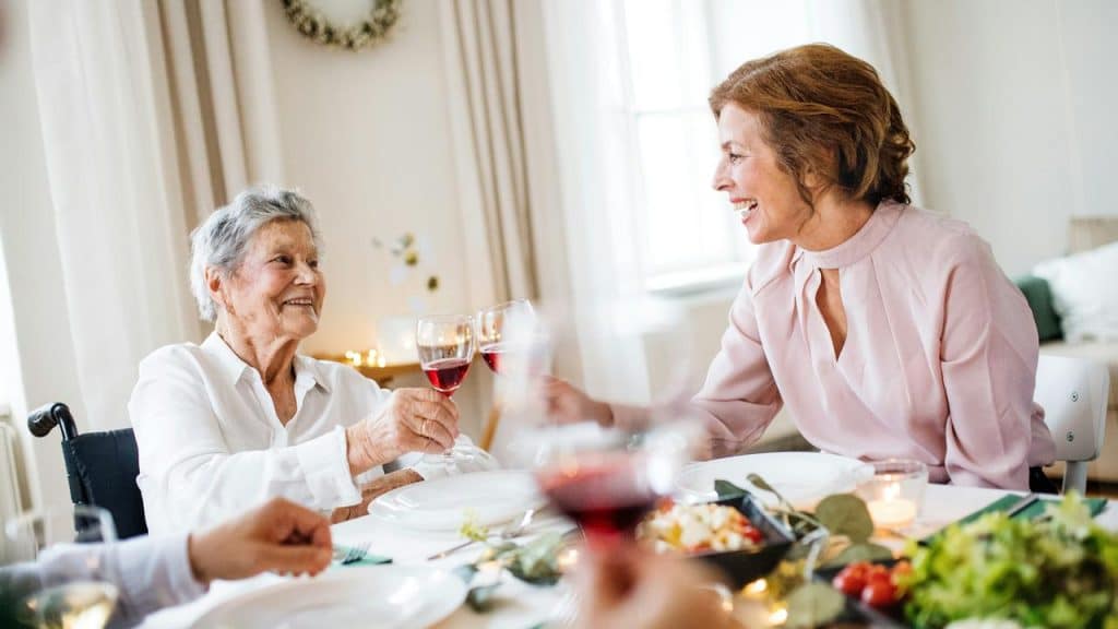 A group of older women smiling and clinking wine glasses at a dinner table.
