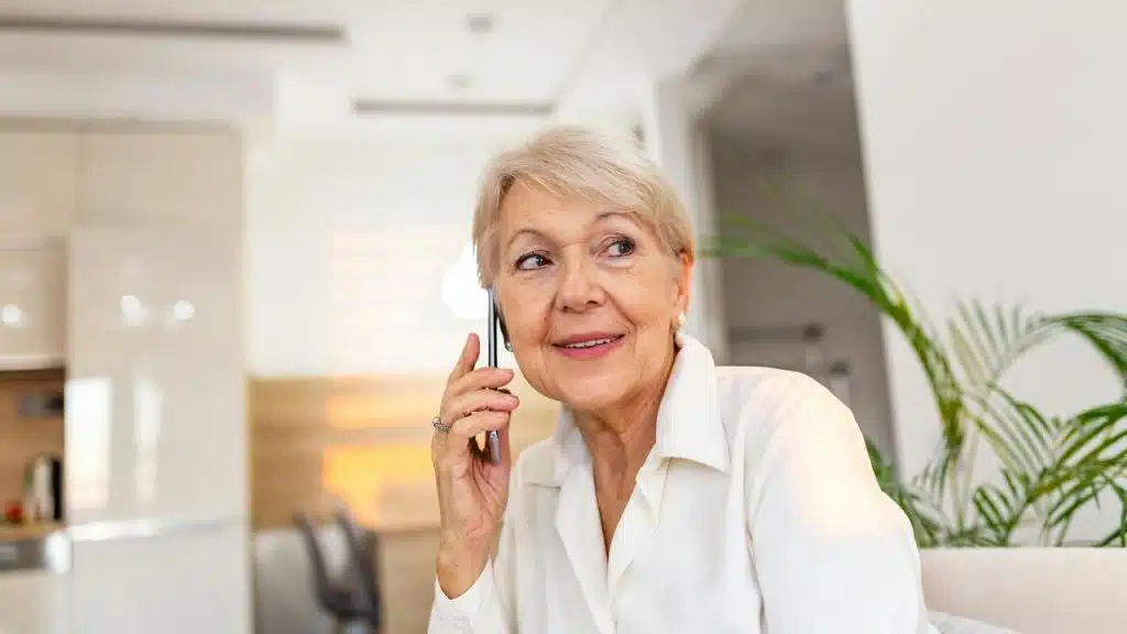 An older woman sitting on a couch and talking on her phone.