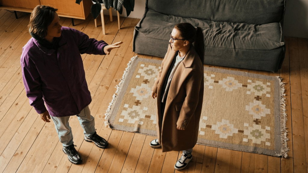 An overhead view of two people standing on a rug, one gesturing with a raised hand.