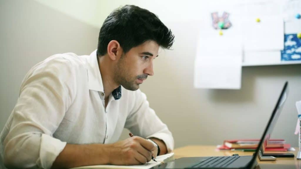 A man reviewing financial documents on his laptop at a desk.