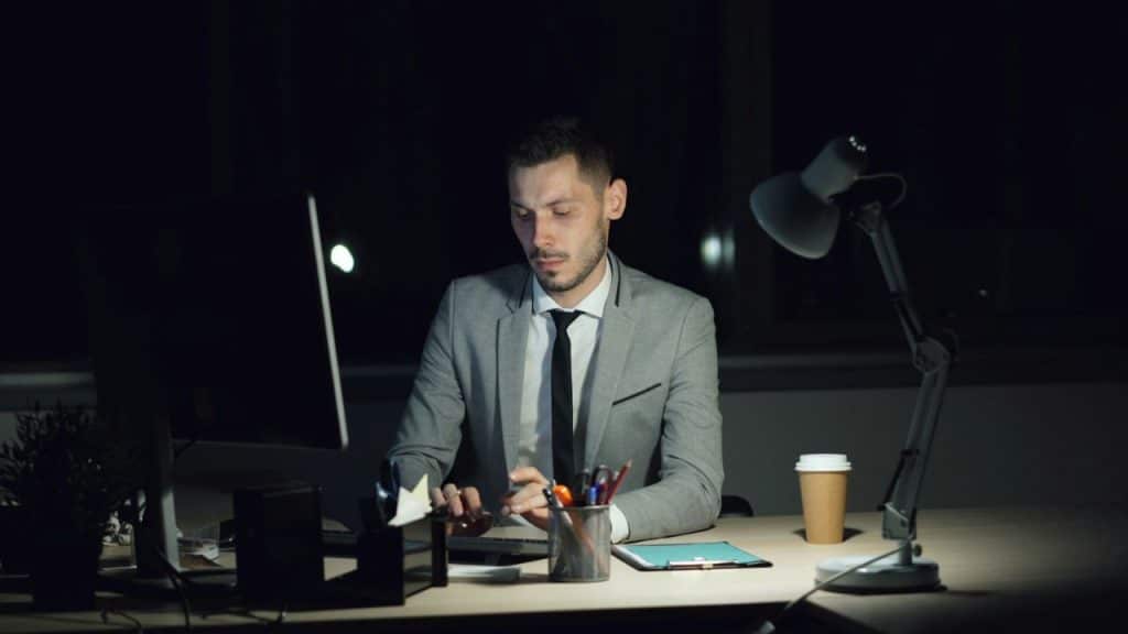 A focused businessman in a gray suit works at his desk in a dark office.