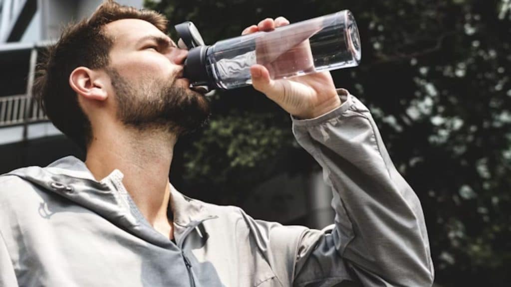 A man drinking water outdoors after finishing a workout