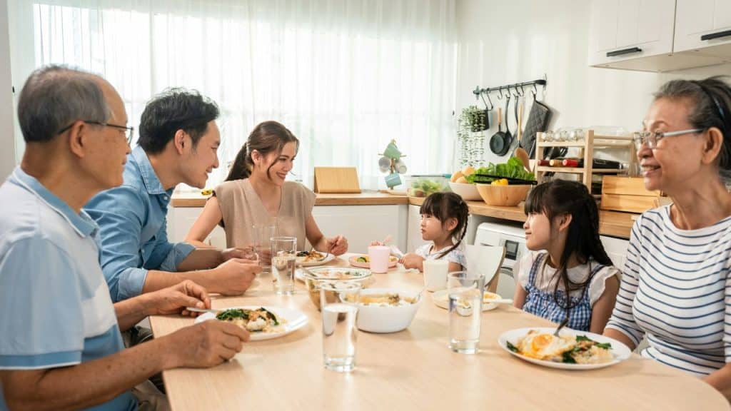 A happy, multi-generational Asian family is eating and chatting around a wooden table.