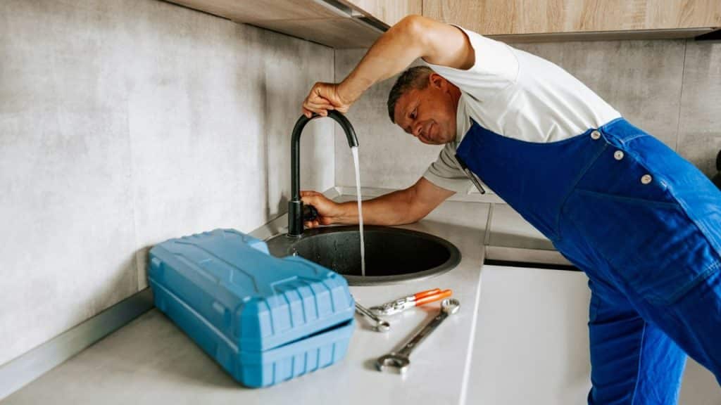 A plumber in blue overalls tests a kitchen faucet he just installed or repaired.
