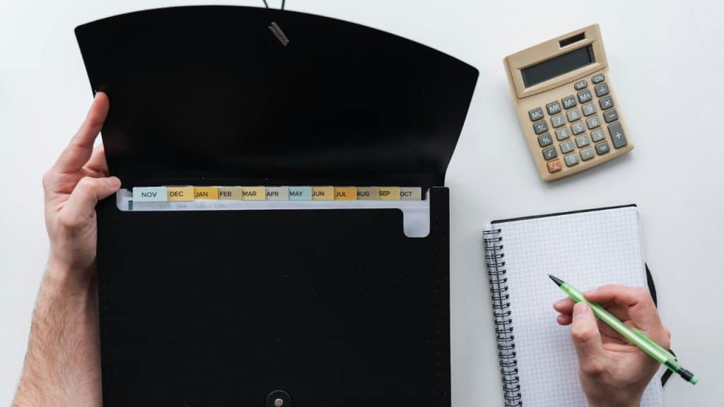 An overhead shot of a person opening a black file folder with monthly tabs next to a calculator and notebook.