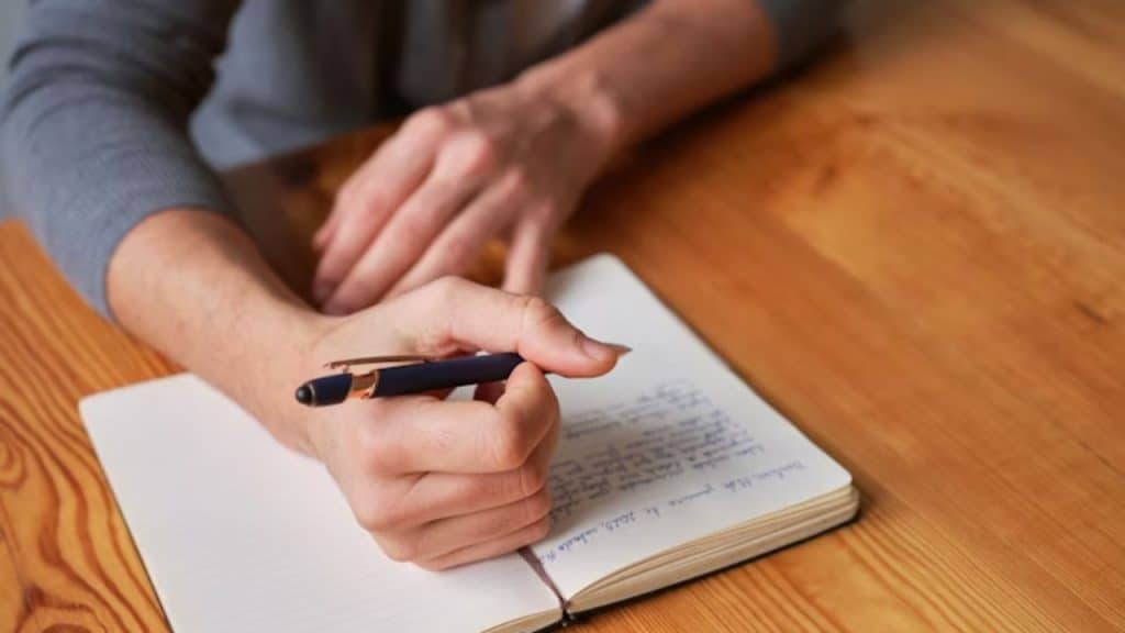 A man writing in a journal at a wooden desk