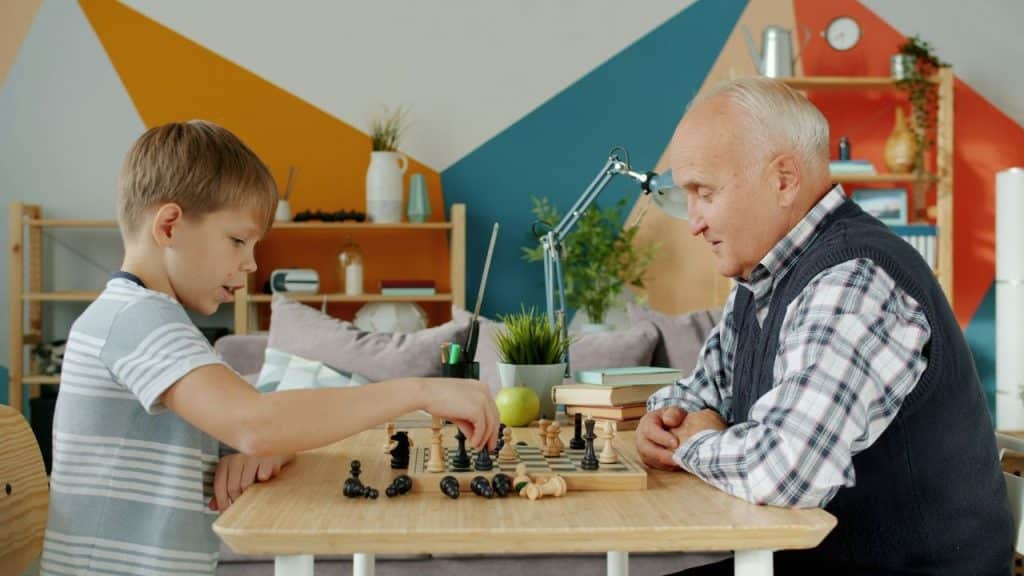 A young boy and an elderly man in a plaid shirt play a game of chess in a brightly decorated room.