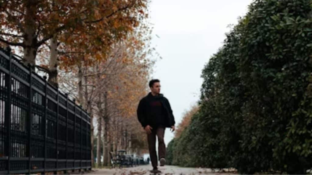 A man walking through a park with colorful autumn leaves