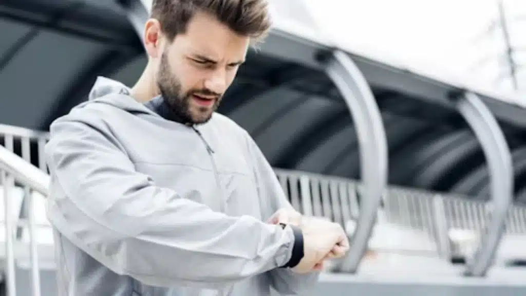 A man checking his smartwatch while walking outdoors in sportswear