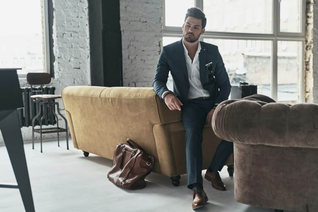 The man is looking away while leaning on a sofa.